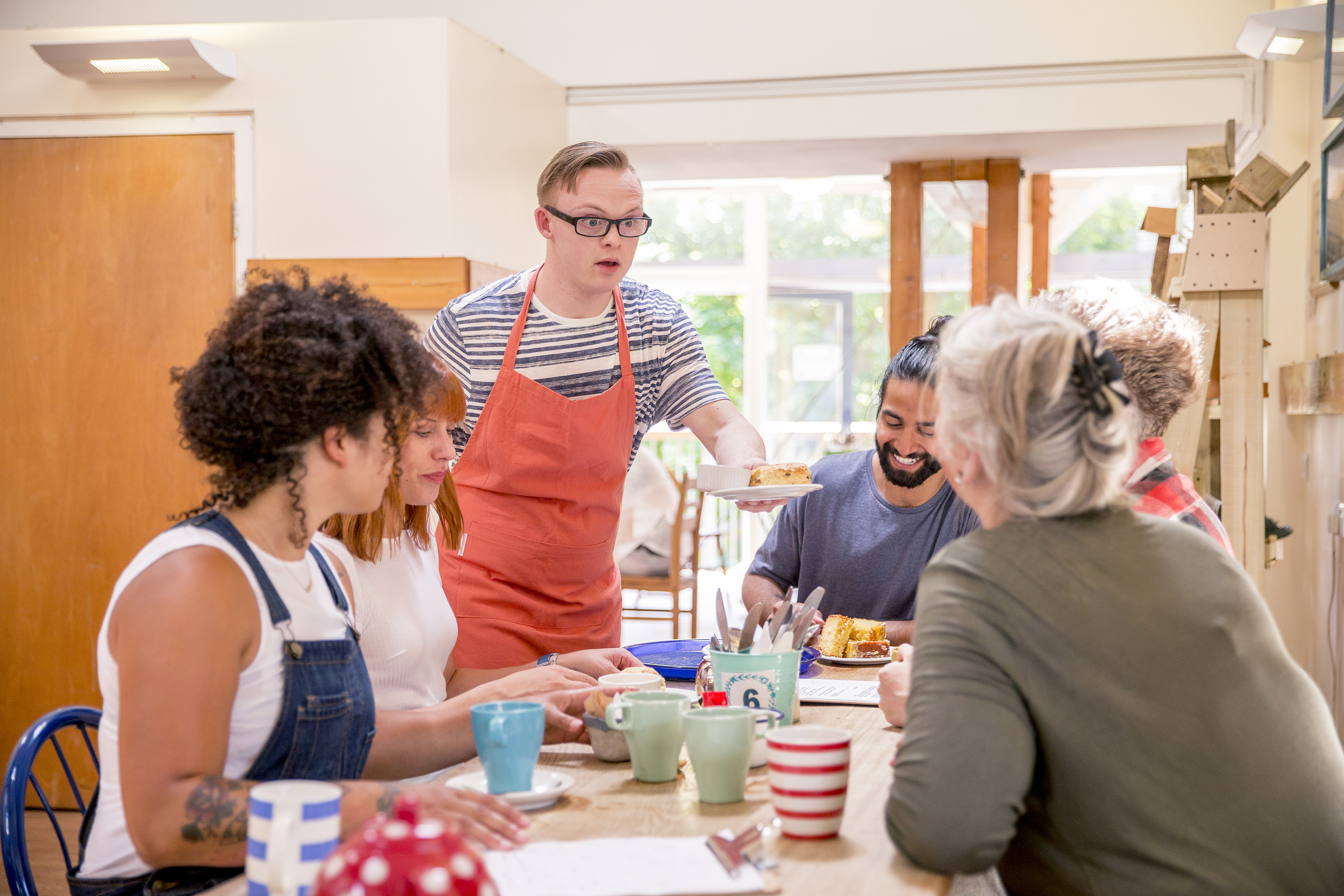 Young male adult serving caje to a table of people in a cafe